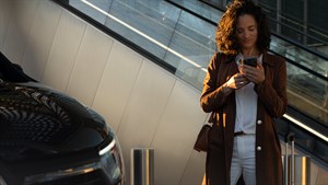 Žena stoji pored automobila i koristi mobitel.